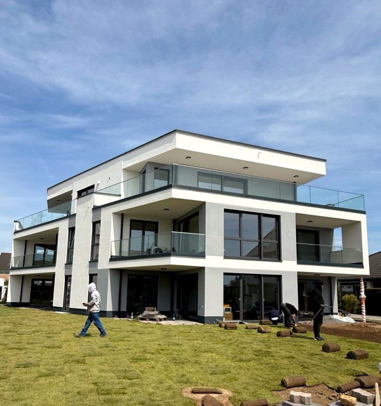 Eines der beiden Mehrfamilienhäuser von der Gartenseite, mit umlaufenden Balkonen und Glasgeländern